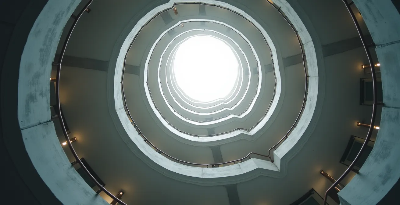 Vue en contre-plongée d'un escalier monumental en spirale dans un bâtiment moderne avec lumière naturelle zénithale